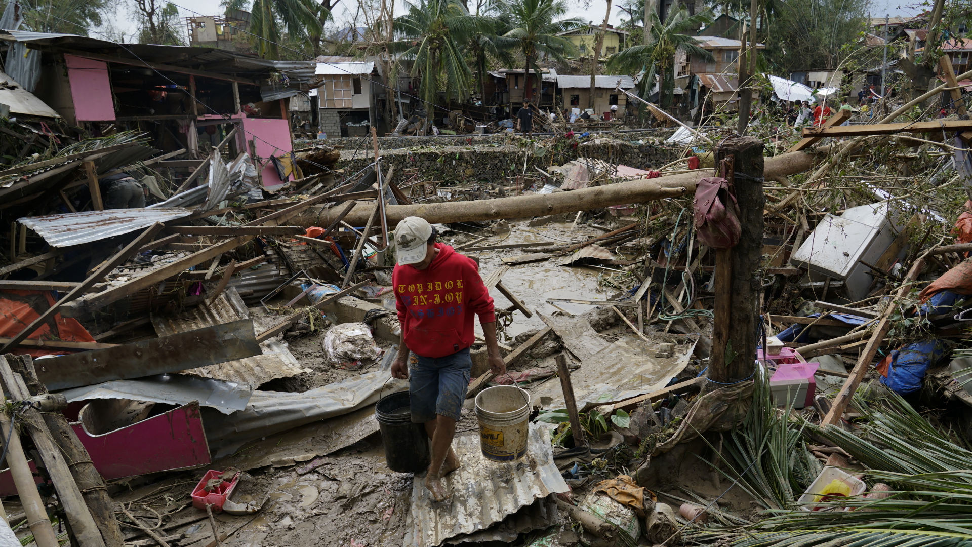 Ein Mann trägt Eimer in einer durch den Taifun "Rai" verwüsteten Region.  | dpa