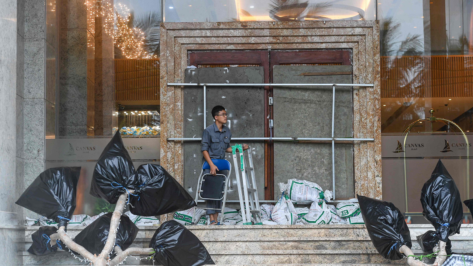 Ein Mann legt Sandsäcke vor den mit Brettern gesicherten Eingang eines Hotels. | AFP