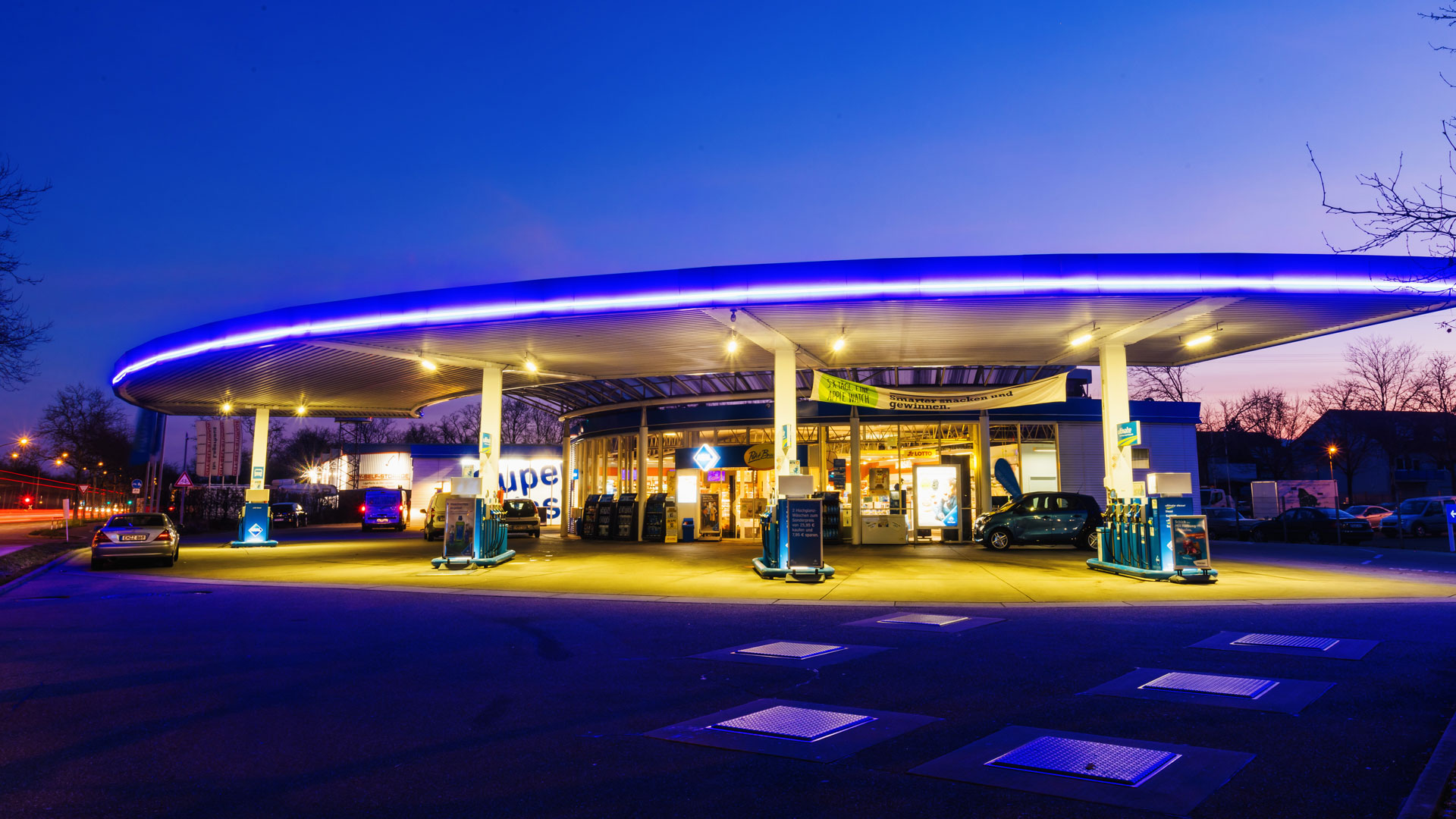 Eine nahezu leere Tankstelle ist blau beleuchtet während im Hintergrund die Sonne aufgeht.  | picture alliance/dpa