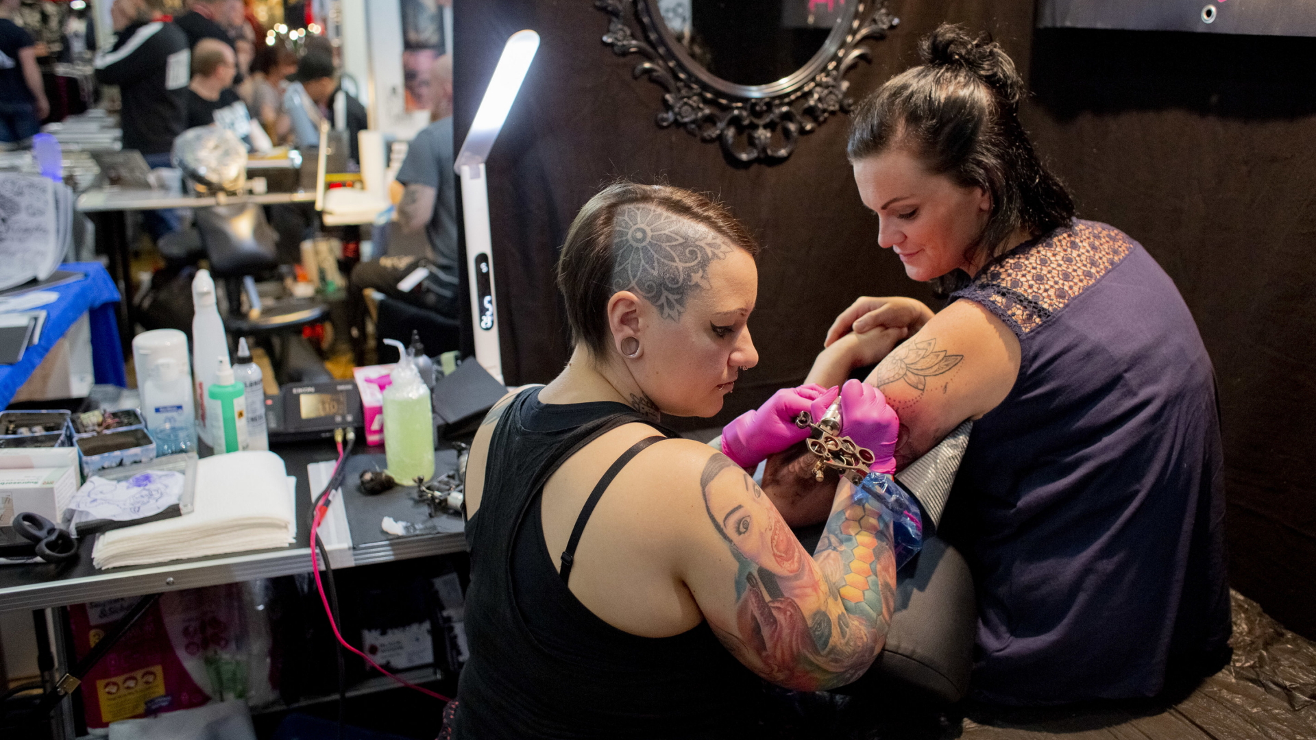 Eine Tattoo-Künstlerin mit einem Tattoo auf dem Kopf tätowiert eine Besucherin auf der 10. Tattoo Convention in Erfurt. (Archiv) | dpa