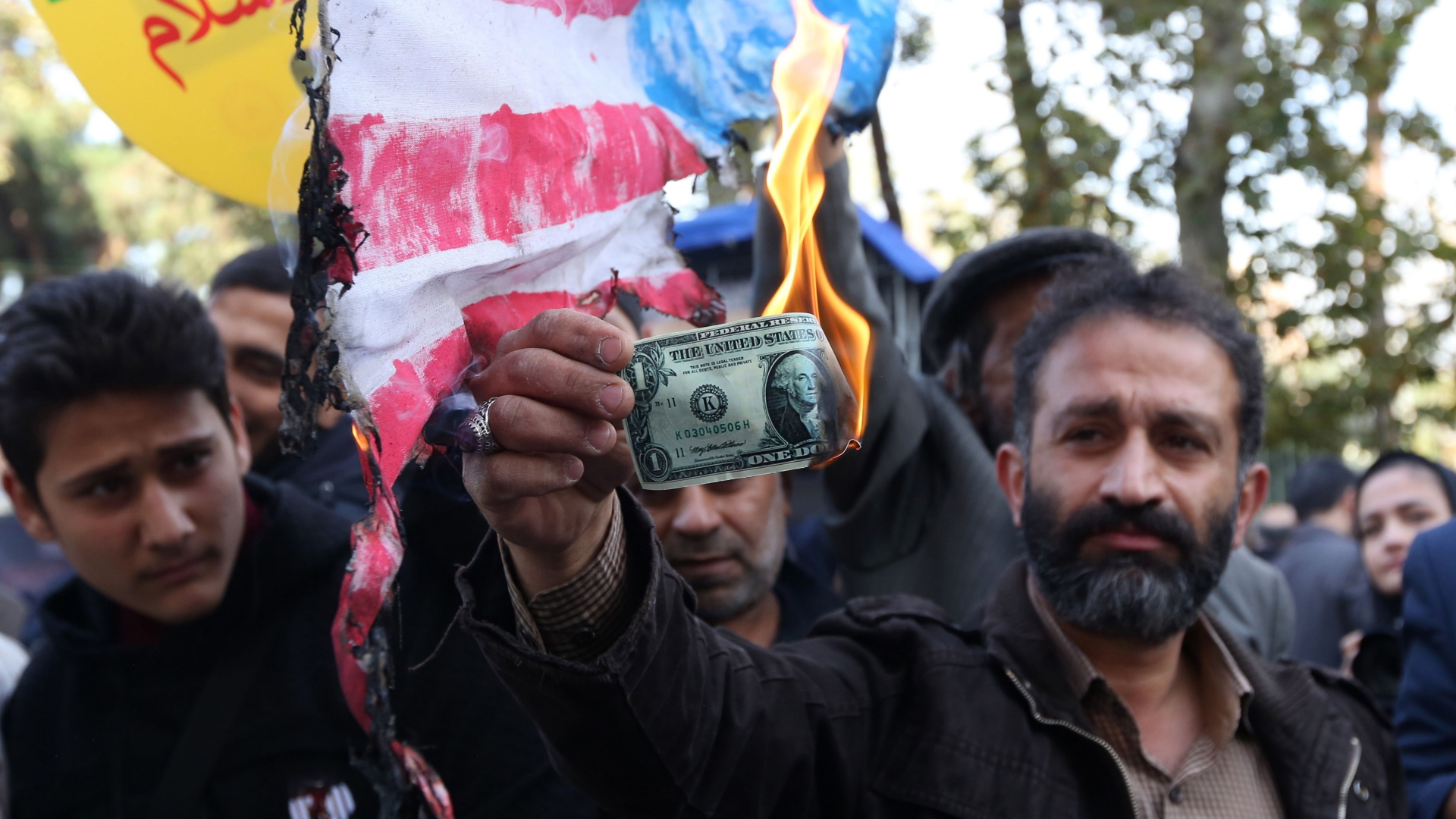 Ein Mann hält in Teheran einen brennenden Dollarschein hoch. | Bildquelle: AFP
