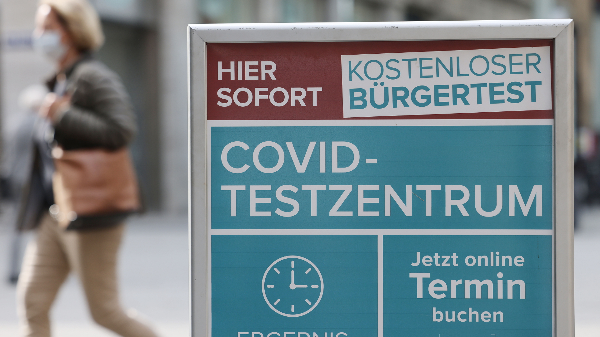 Eine Frau geht an einem Hinweisschild für ein Covid-Testzentrum in Köln vorbei. | dpa