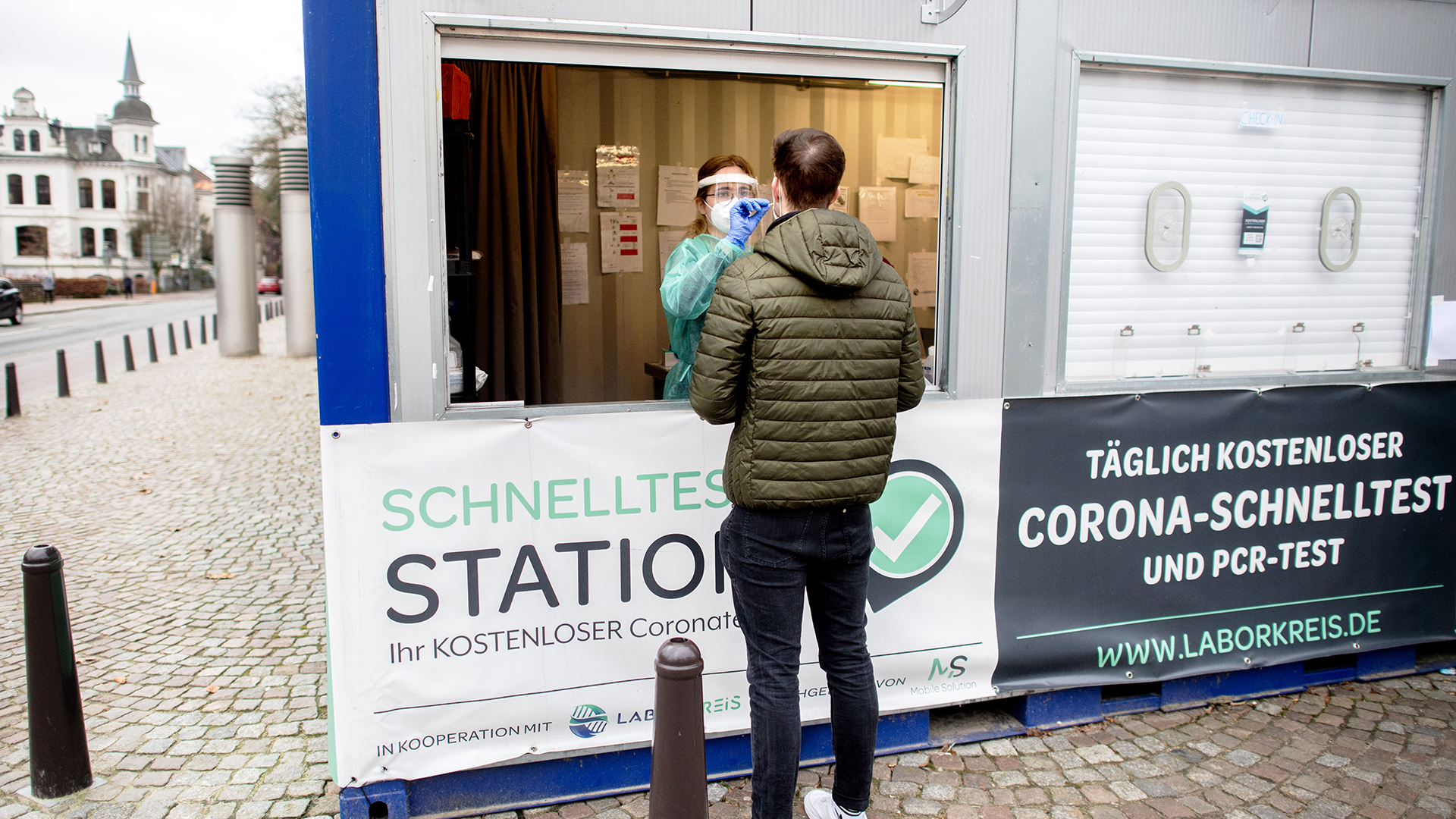 Menschen warten vor einem Corona-Testzentrum in der Bad Homburger Innenstadt auf ihren kostenlosen Covid-Test. | dpa