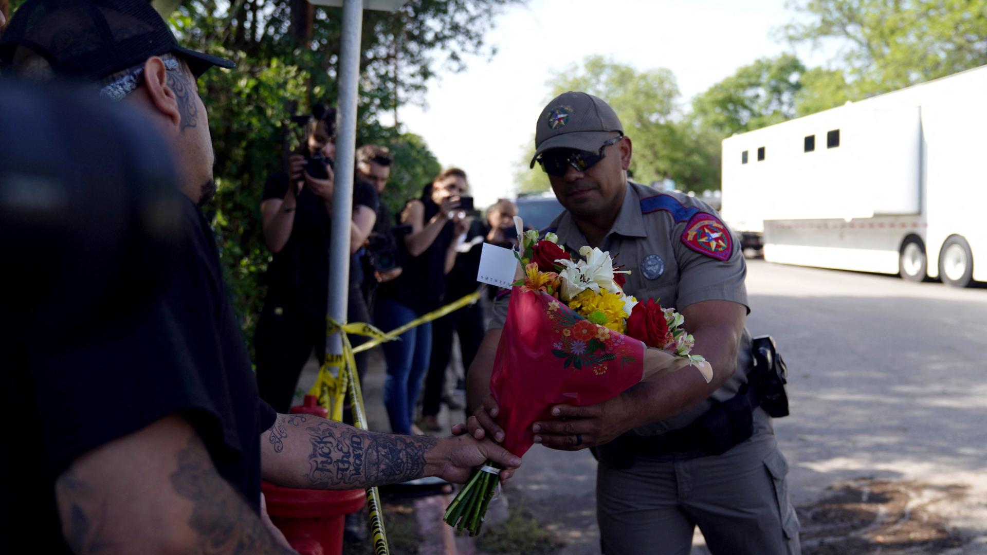 Ein US-Polizist nimmt Blumen von einem Mann entgegen, um sie an der Grundschule in Uvalde, Texas abzulegen, an der zuvor 21 Menschen erschossen wurden.