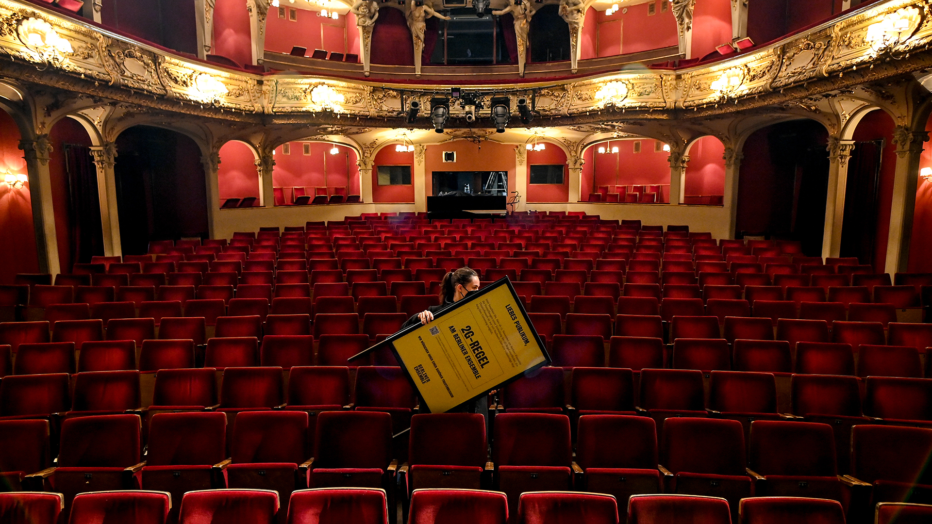 Eine Mitarbeiterin trägt einen Aufsteller mit dem Hinweis auf die 2G-Regel durch den Zuschauerraum des Berliner Ensemble. | picture alliance/dpa/dpa-Zentral