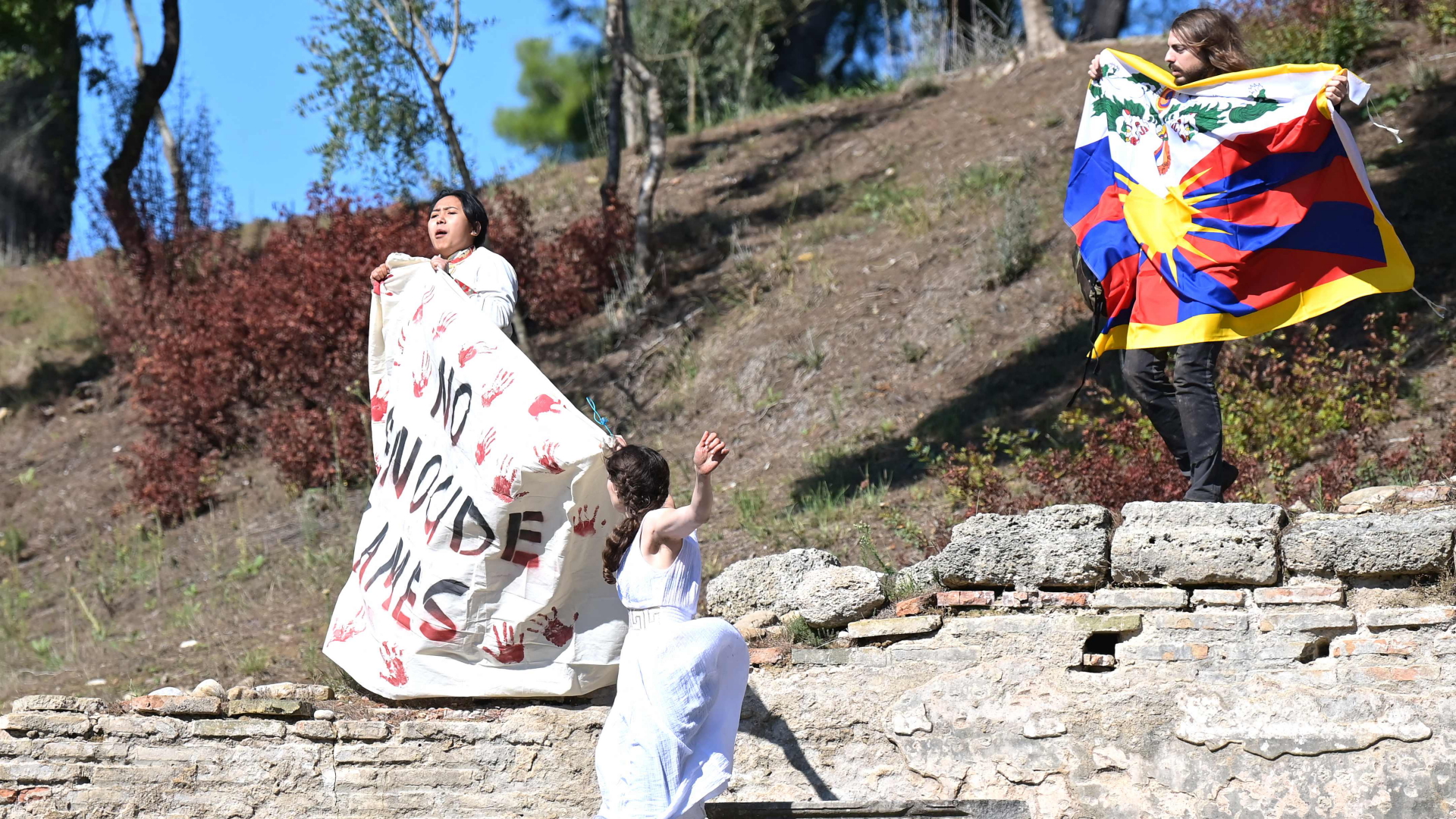 Aktivisten halten bei der Entzündung des Olympischen Feuers eine Tibet-Flagge und ein Plakat mit der Aufschrift "No Genocide Games" (Keine Genozidspiele) hoch. | AFP