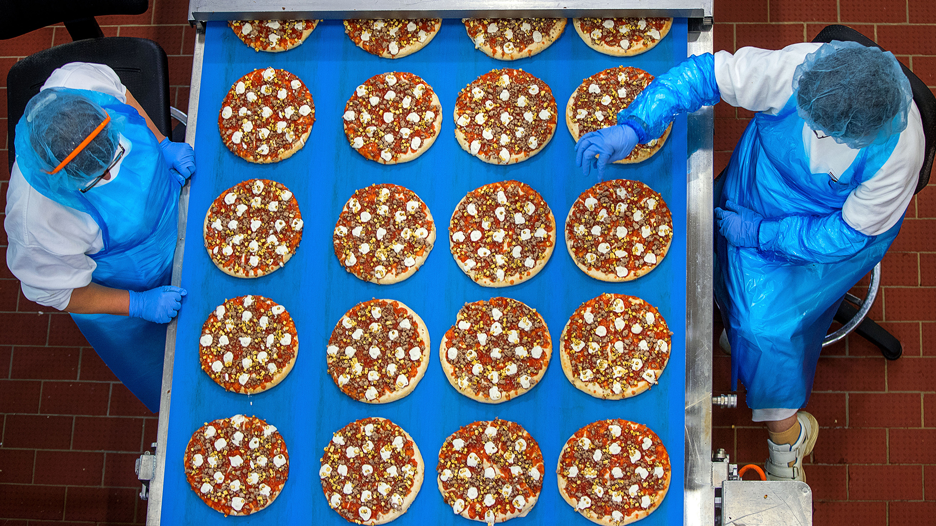 Mitarbeiterinnen kontrollieren in einem Pizzawerk die gleichmäßige Verteilung des Belags auf Pizzen für die Tiefkühltruhe | dpa