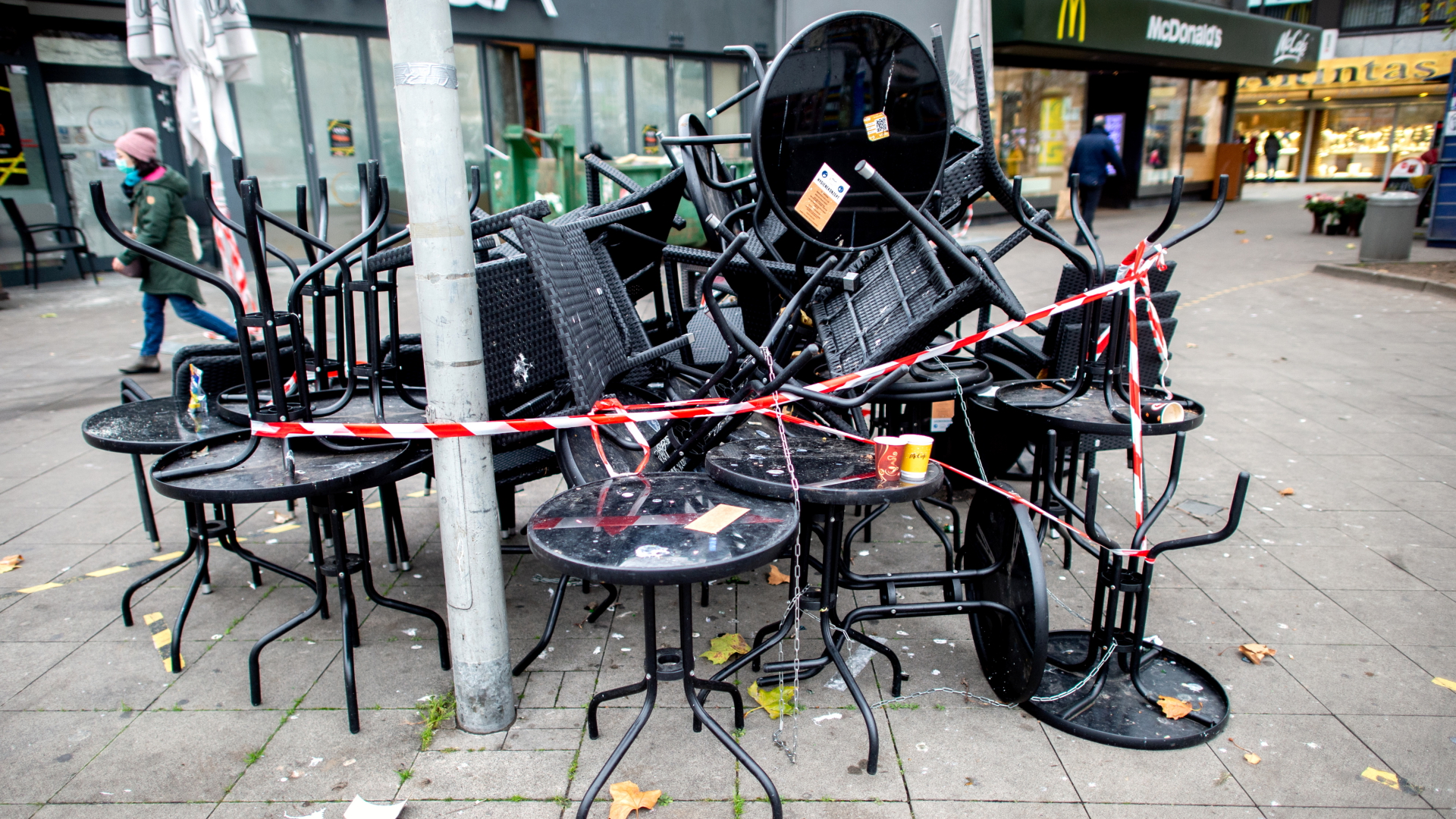 Tische und Stühle stehen übereinander gestapelt und abgesperrt vor einem geschlossenen Restaurant in der Innenstadt von Hannover. | dpa