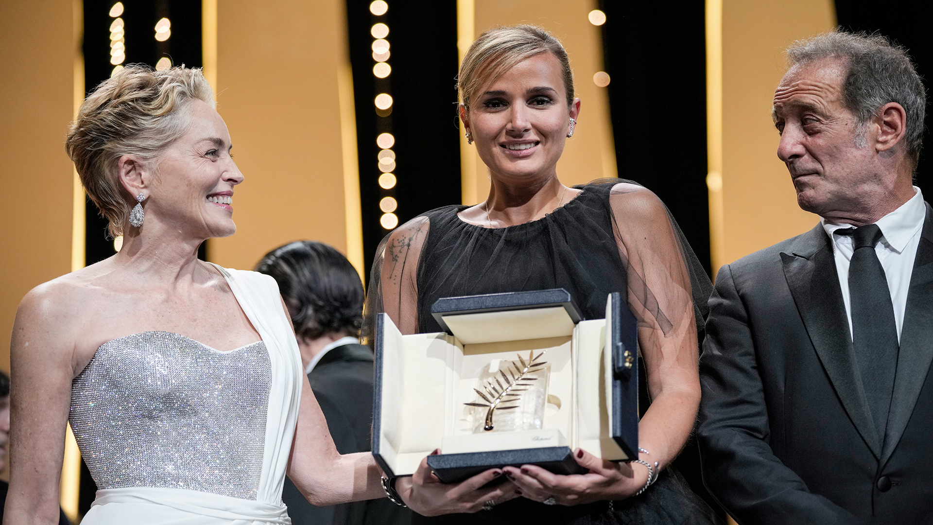 Julia Ducournau nimmt neben Sharon Stone und Vincent Lindon die Goldene Palme für den Film «Titane» während der Preisverleihung der Filmfestspiele in Cannes entgegen. | dpa