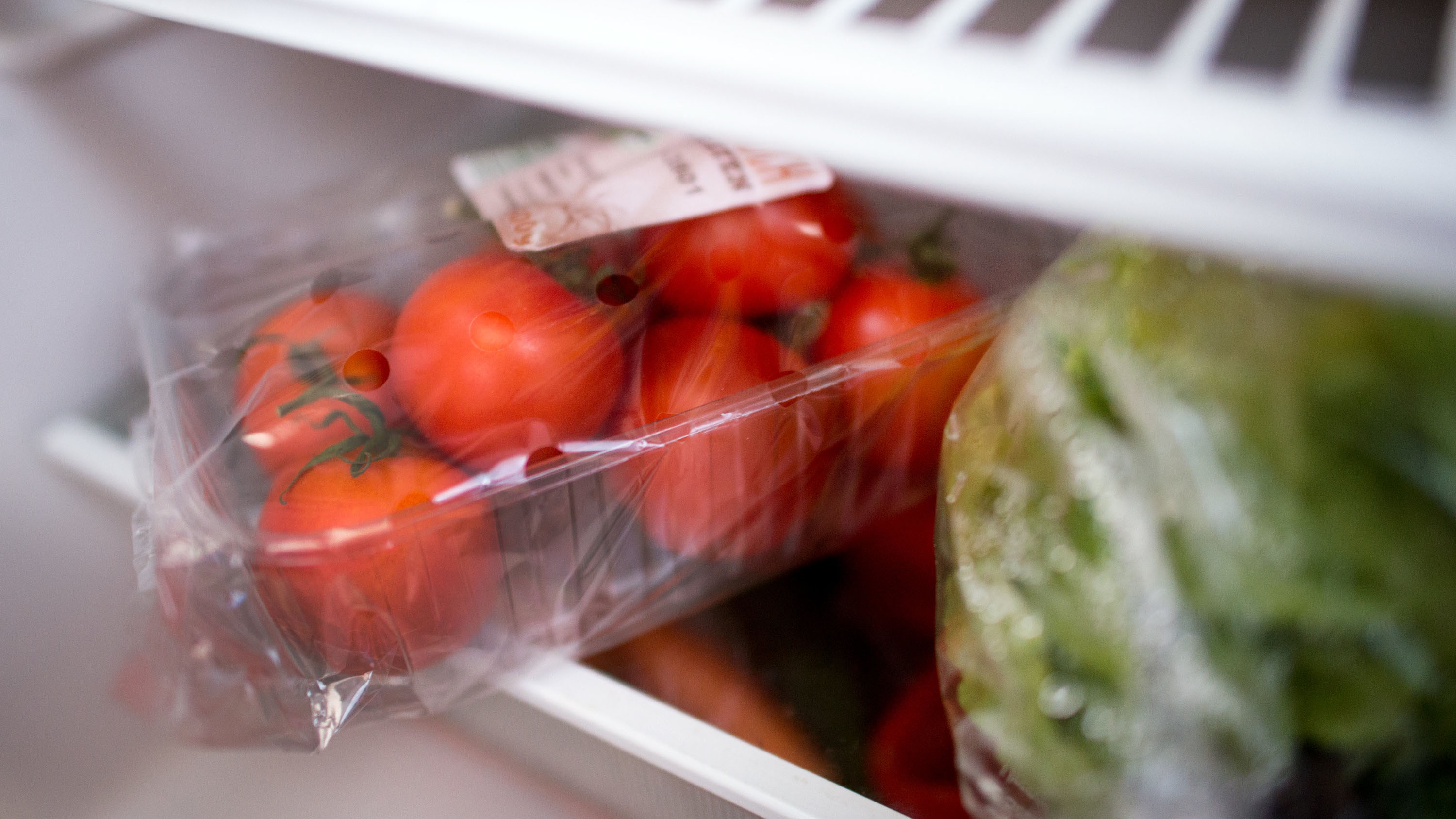 In Plastik verpackte Tomaten liegen in einem Kühlschrank.