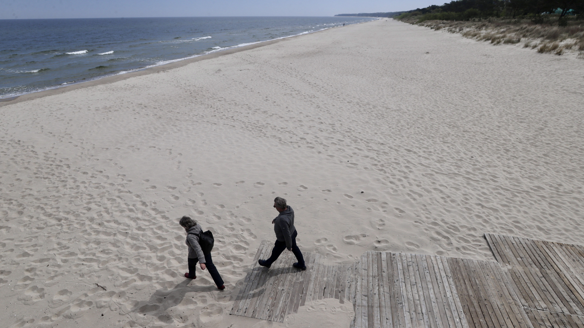 Zwei Touristen an einem sonst leeren Strand an der Ostsee