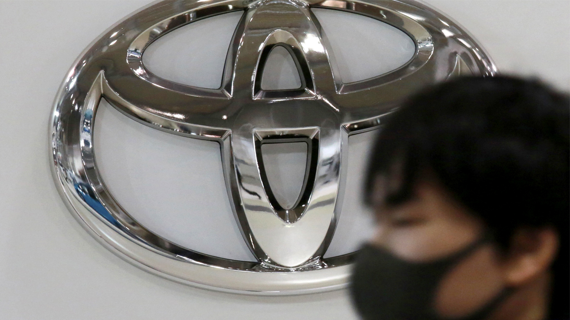 Ein Mann mit Maske vor dem Logo von Toyota | AP
