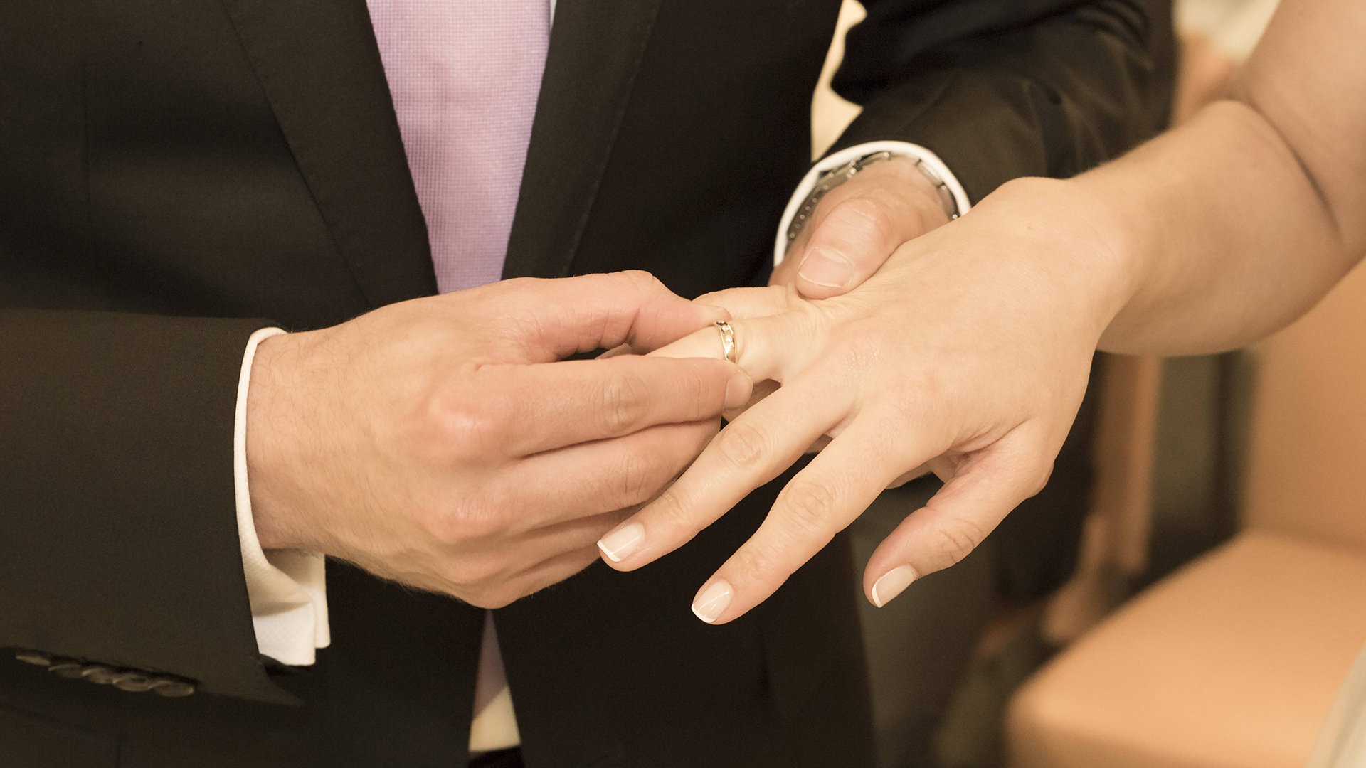 Ein Bräutigam setzt seiner Braut den Ehering auf.