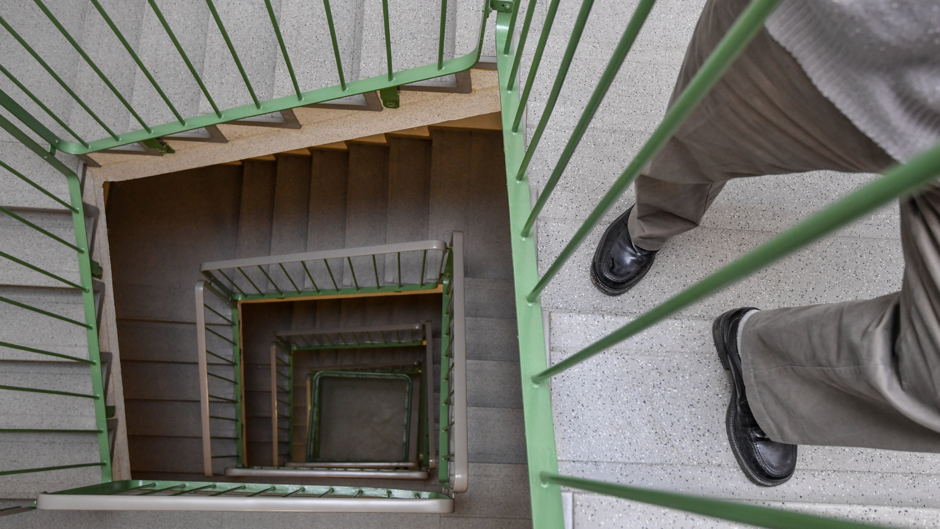 Ein Rentner steht auf der Treppe eines Hausflurs.