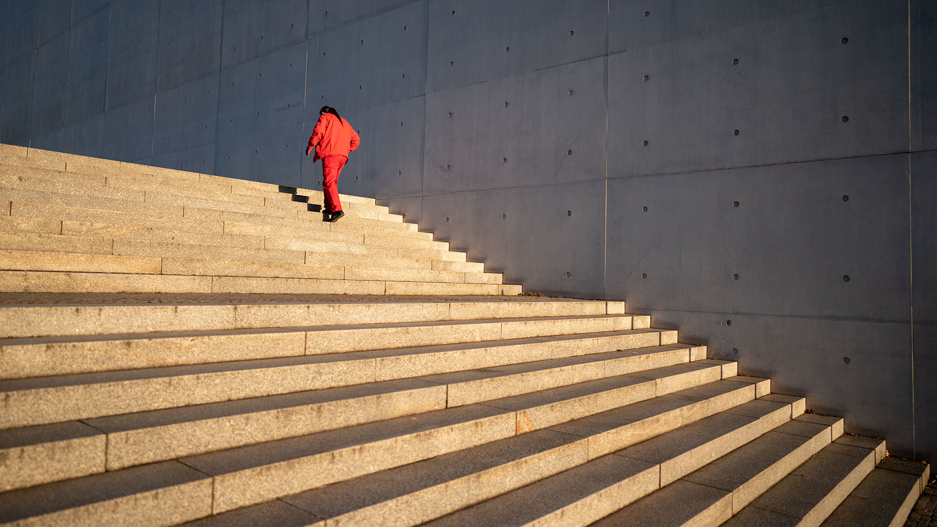 Ein Mann in einem roten Overall geht am Morgen in Berlin im Regierungsviertel die Treppen zum Paul-Löbe-Haus hinauf. | dpa