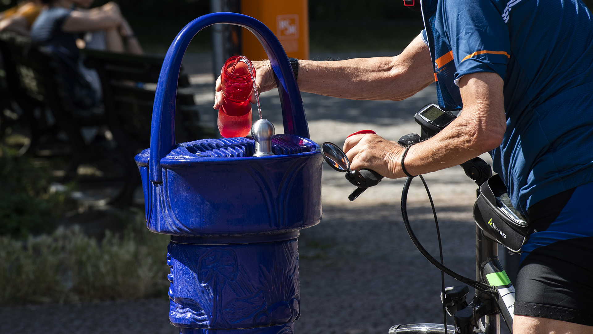 Ein Mann füllt seine Trinkflasche an einem blauen Trinkwasserbrunnen. | dpa