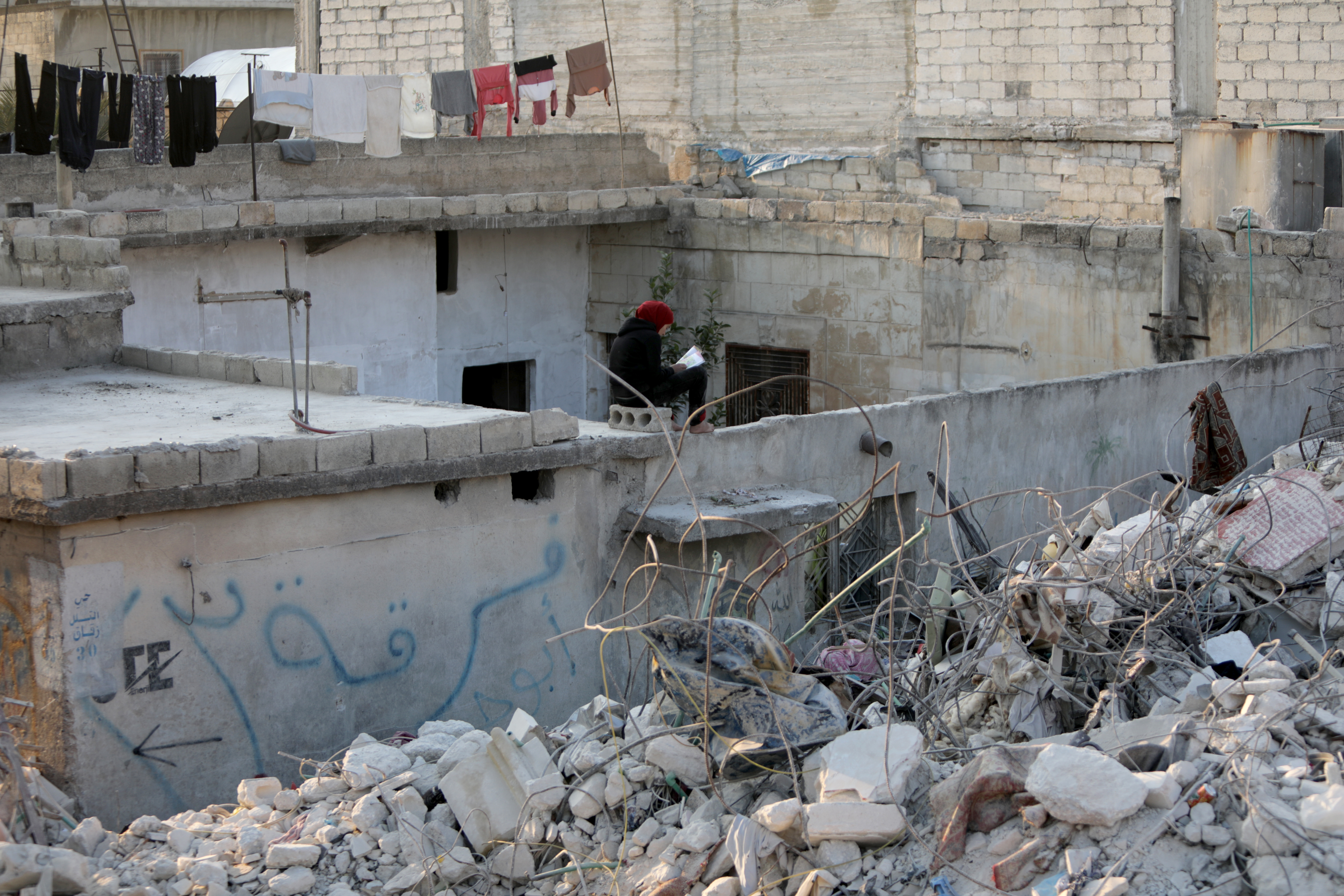 Ein Mensch sitzt in Dschindires auf einer Mauer neben einem zerstörten Haus. (Aufnahme 23.02.2023) | picture alliance / AA
