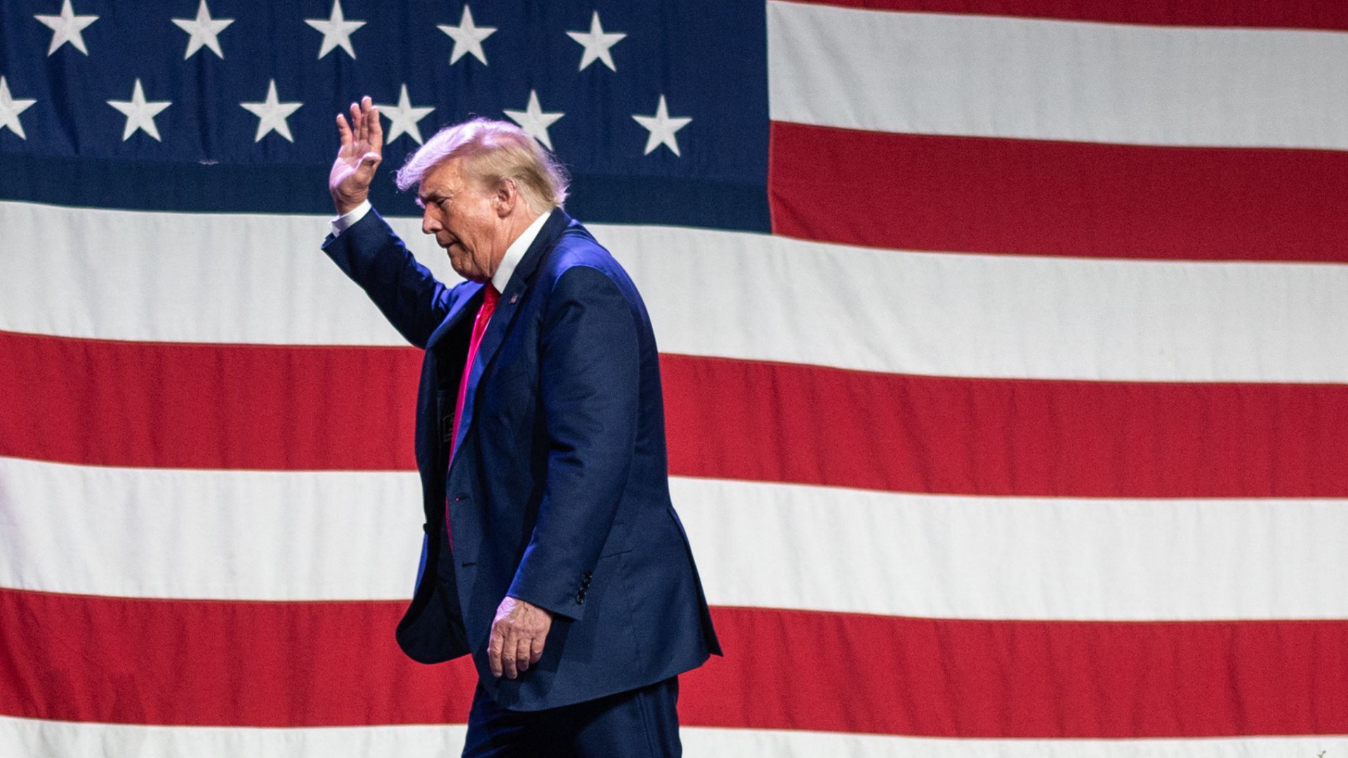 Trump verlässt winkend eine Bühne, auf der eine US-Flagge hängt