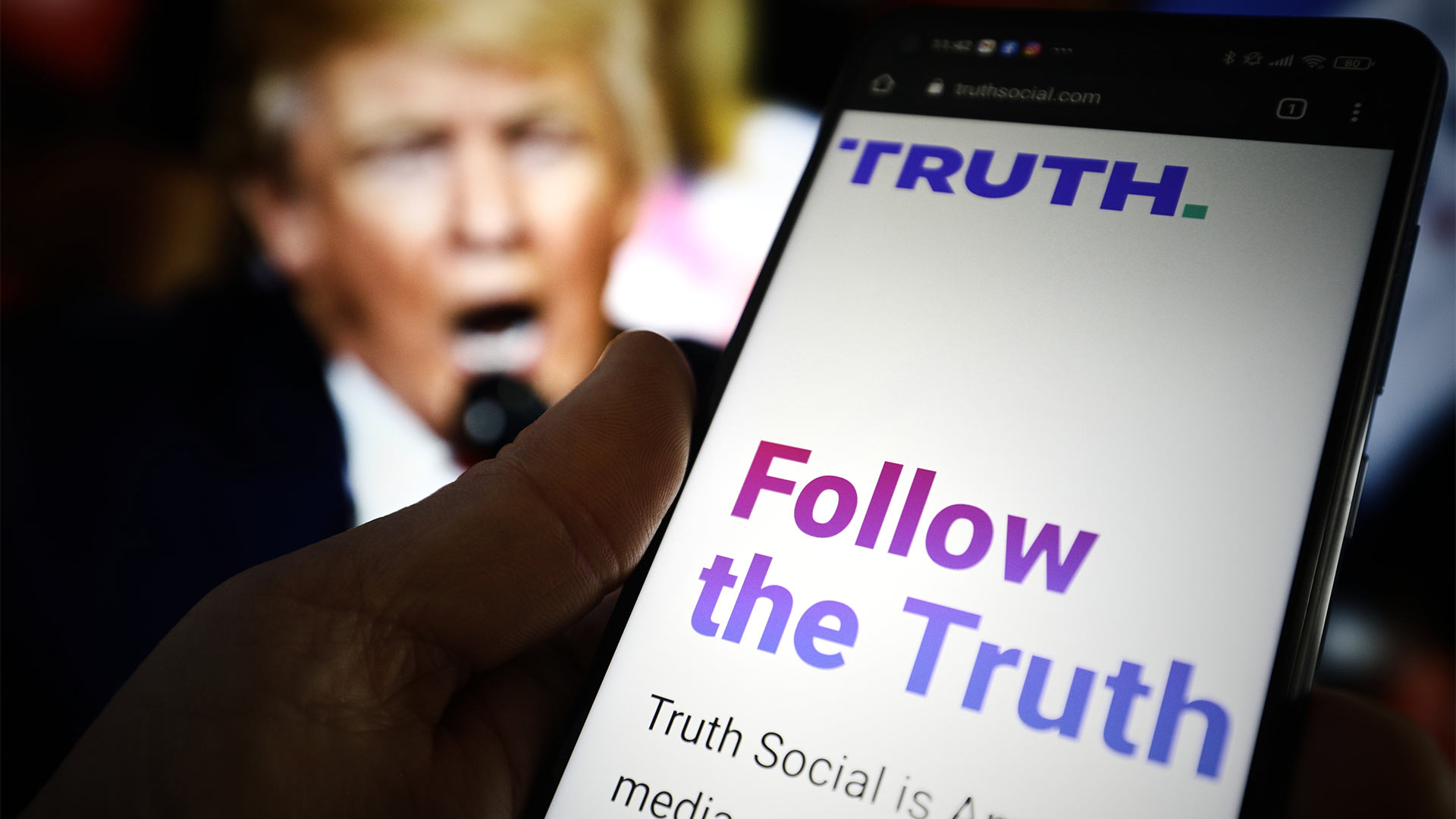 Trumps "Truth Social"-App auf einem Smartphonedisplay vor einem Trump-Portrait