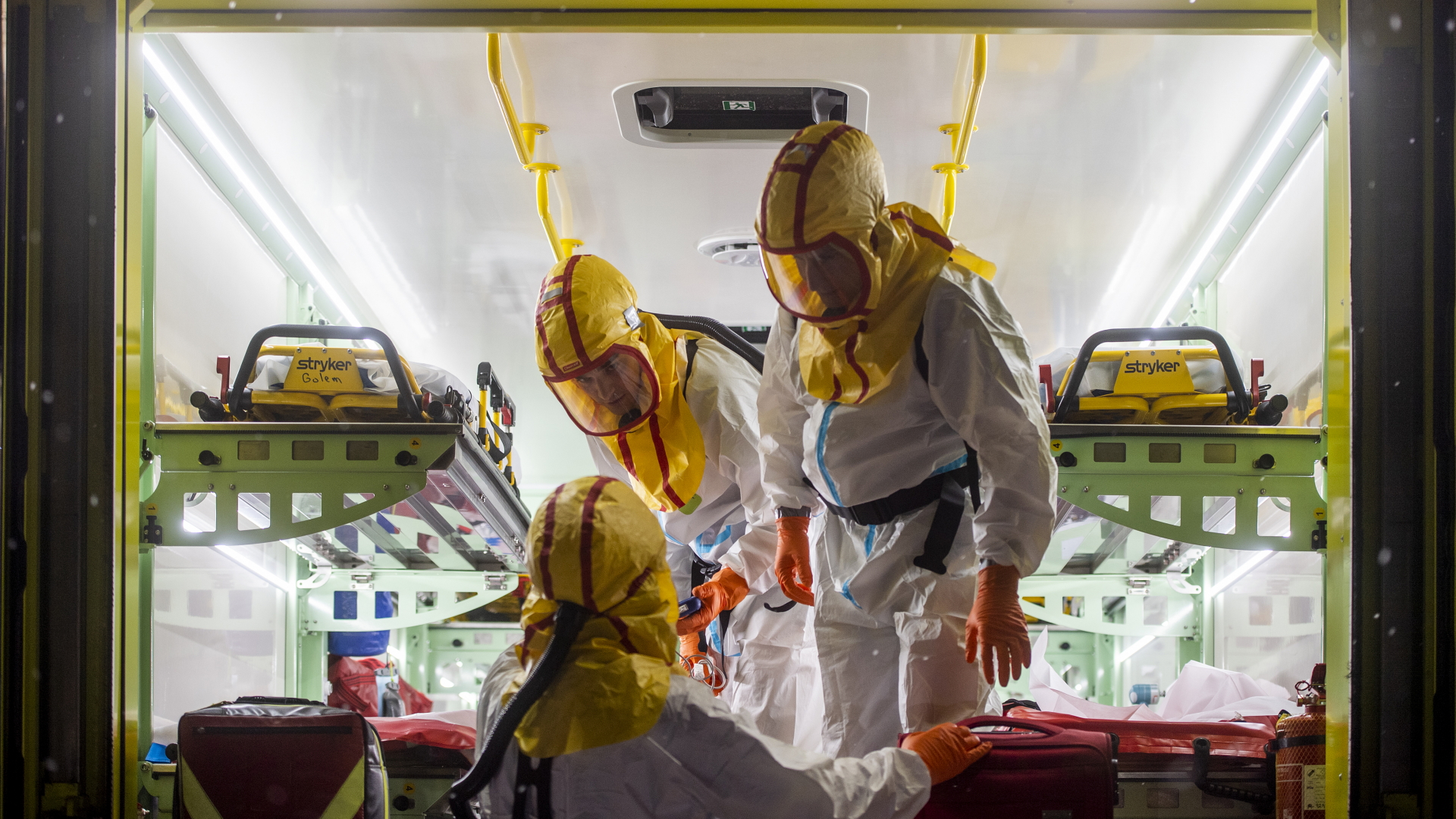 Sanitäter in Schutzkleidung sprechen mit einem Kollegen an der Heckklappe eines Transporters. | dpa