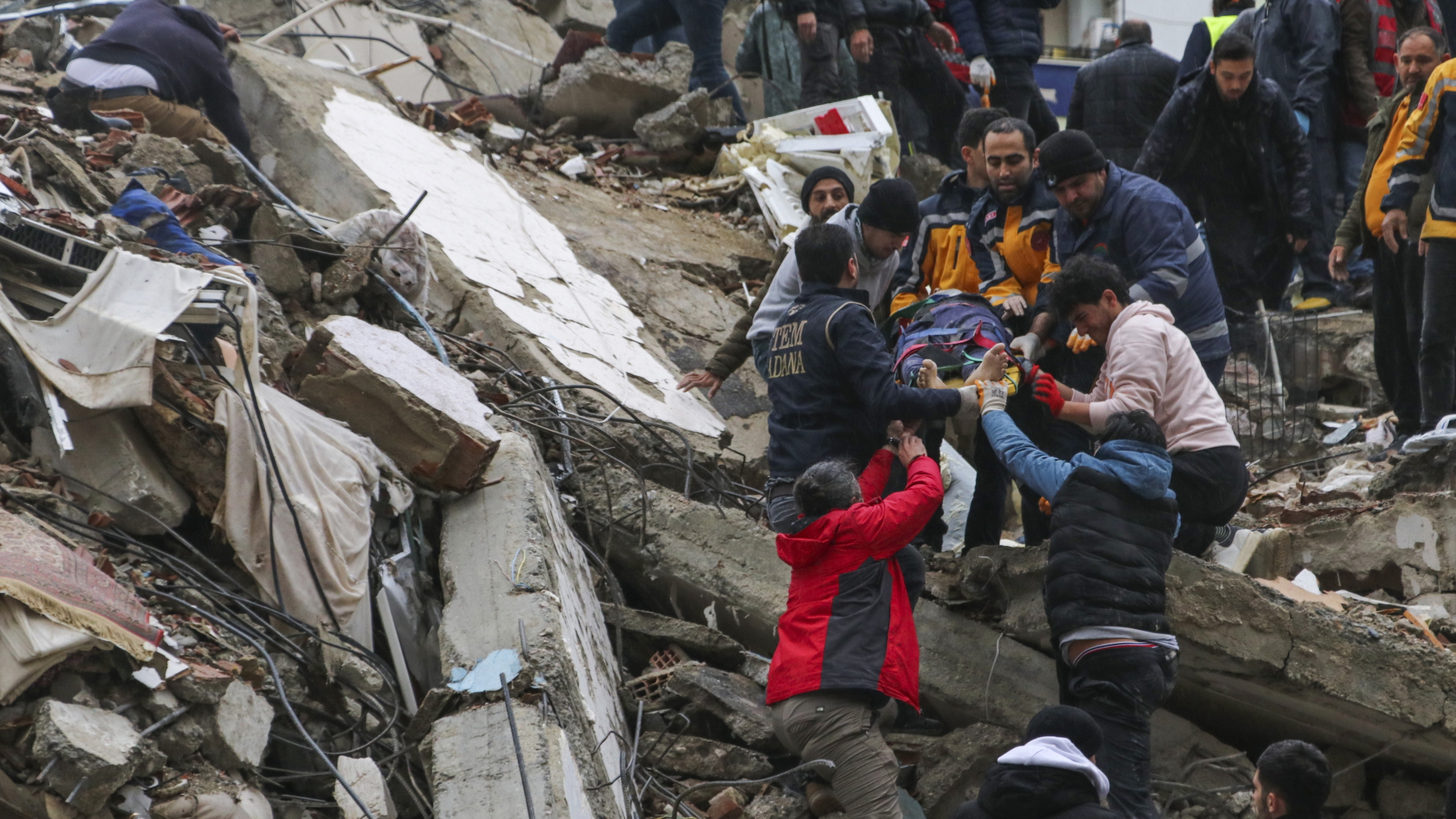 Menschen und Rettungskräfte bergen eine Person auf einer Bahre aus einem eingestürzten Gebäude in Adana
