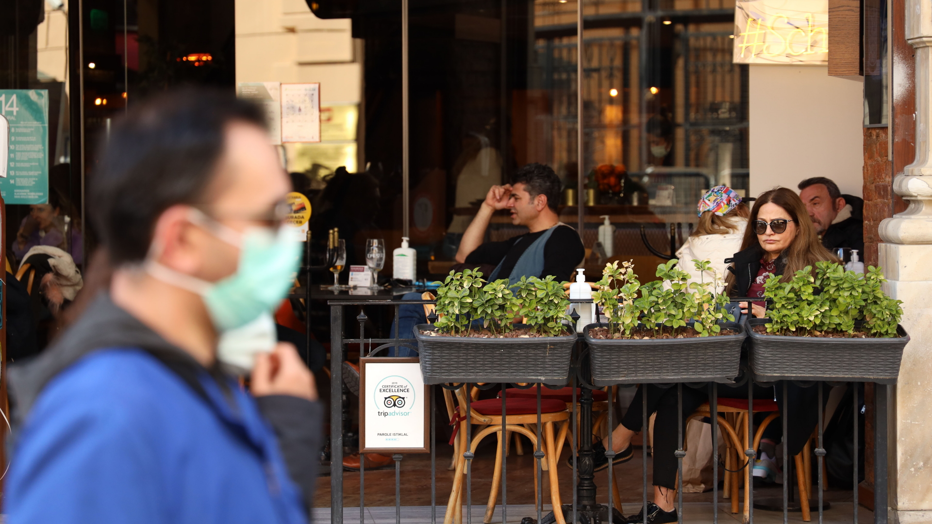  Türkei, Istanbul: Ein Mann mit Mund-Nasen-Schutz läuft an einem Café vorbei, in dem einige Menschen sitzen.  | dpa