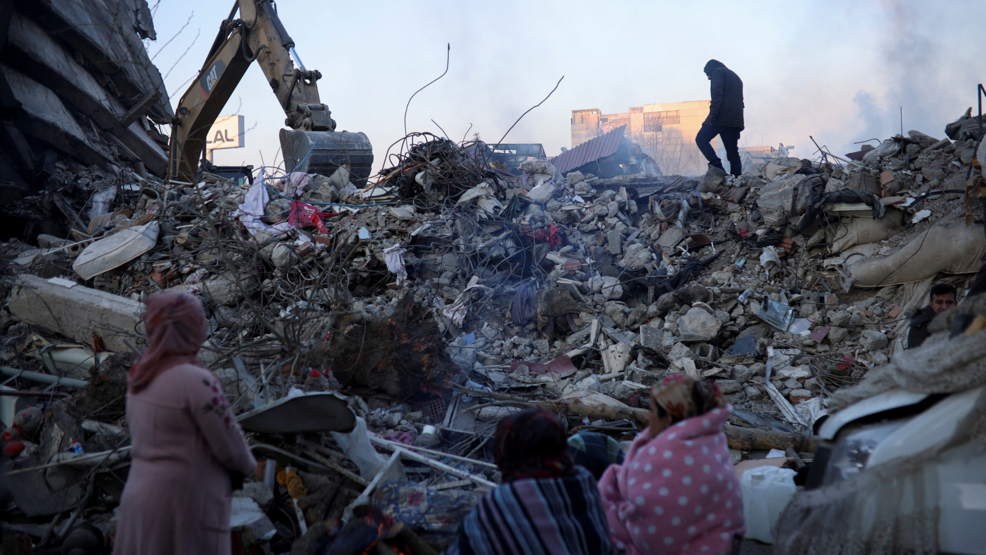 Frauen stehen eingehüllt in Decken vor einem zerstörten Gebäude in der türkischen Stadt Kahramanmaras.