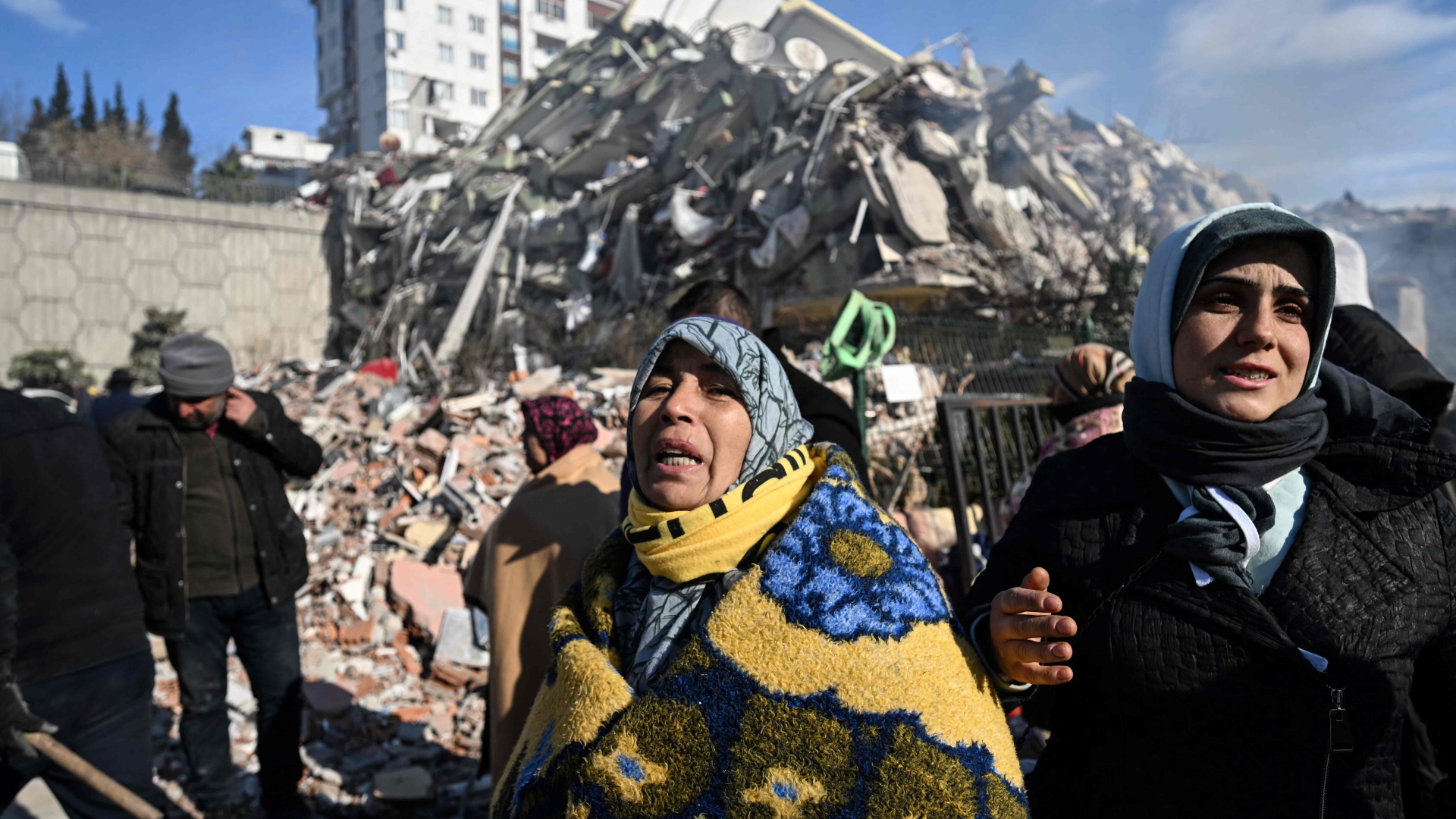 Zwei Frauen schauen in der türkischen Stadt Kahramanmaras verzweifelt in die Kamera, im Hintergrund ein durch das schwere EErdbeben zerstörte Gebäude.