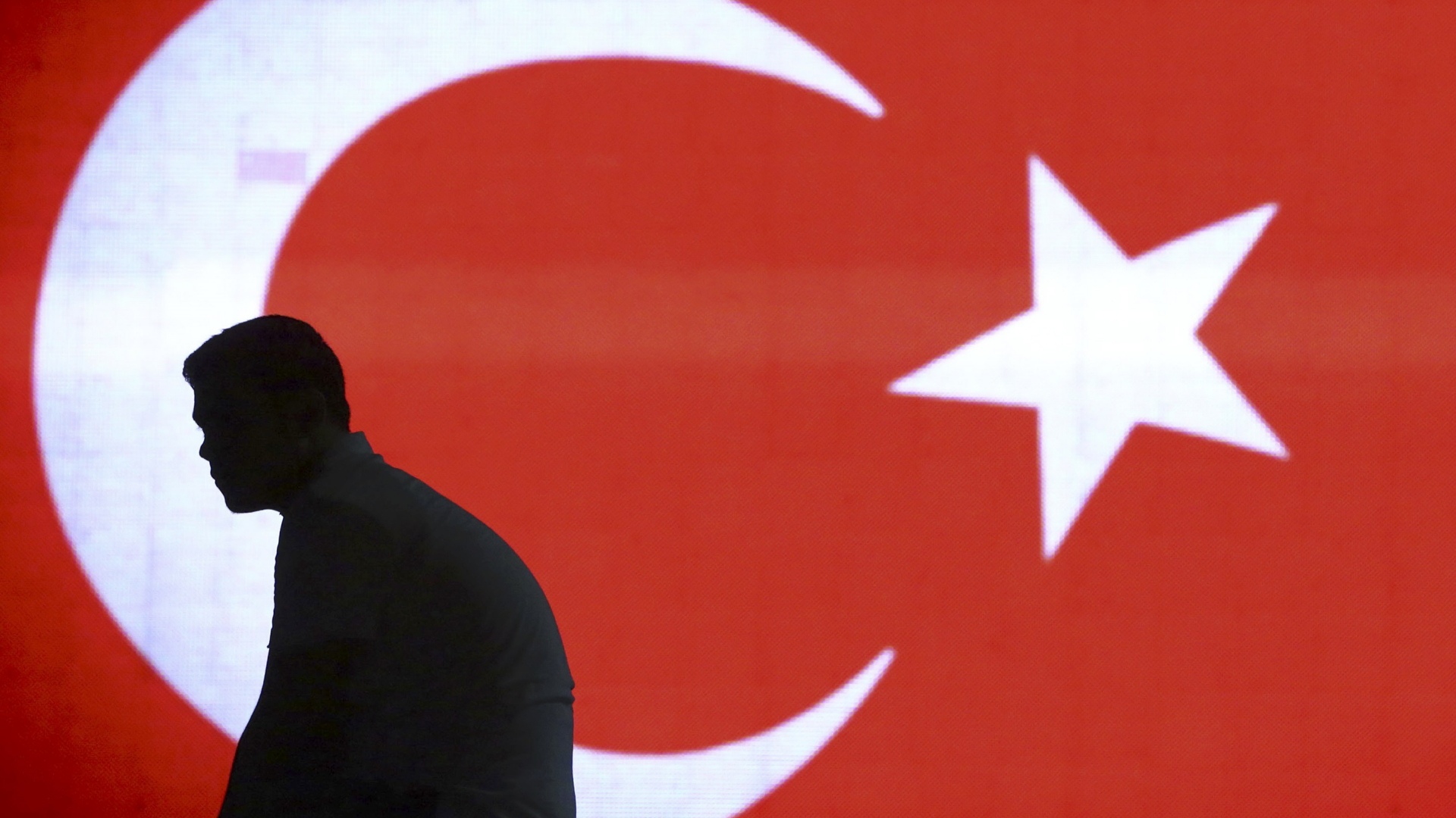 Ein Mann sitzt am Istanbuler Flughafen vor einer türkischen Flagge | null