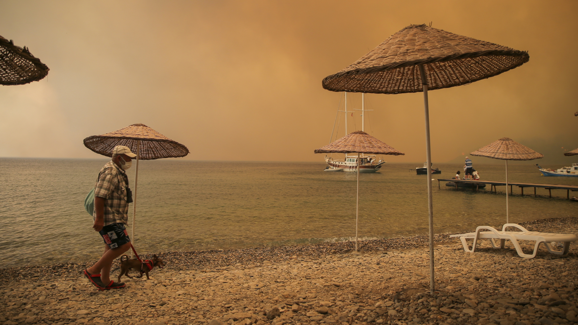  Ein Mann geht mit einem Hund durch rauchverhangene Luft an einem Strand im türkischen Bodrum entlang. | dpa