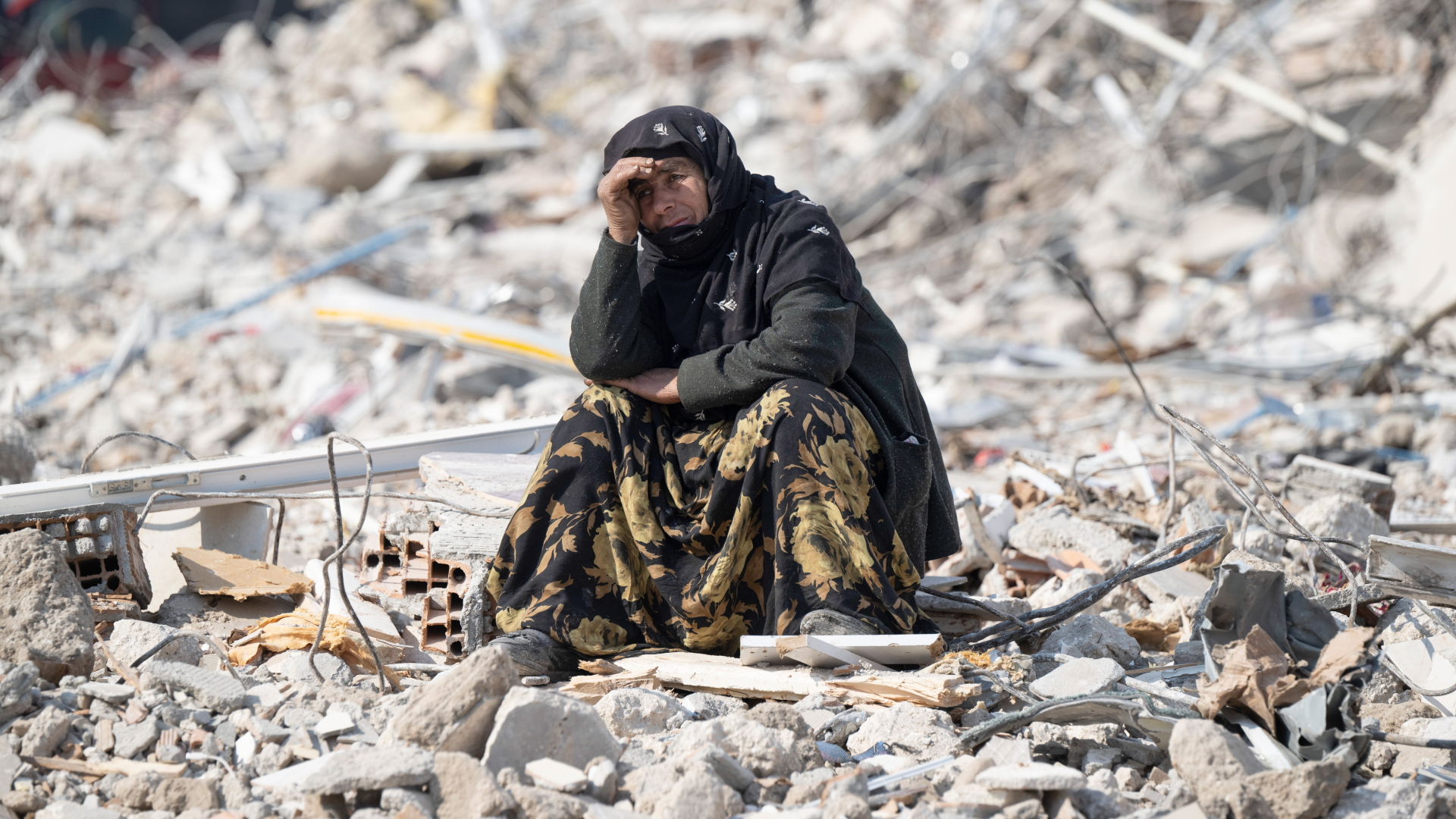 Eine Frau sitzt in Antakya, Türkei, zwischen Trümmern und beobachtet die Bergung von Opfern. | dpa