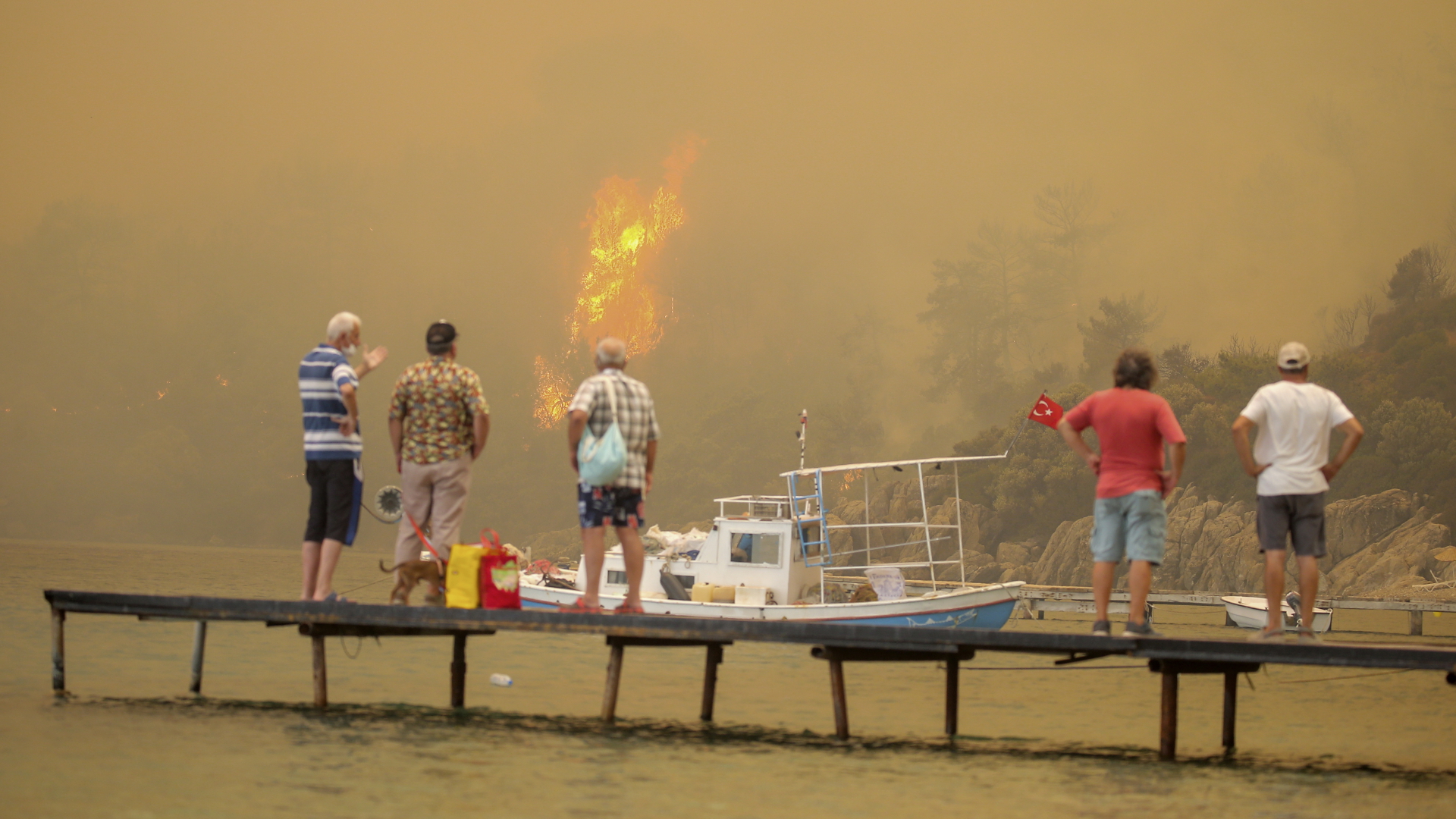 Touristen stehen während eines Waldbrands im türkischen Bodrum auf einem Steg. | dpa