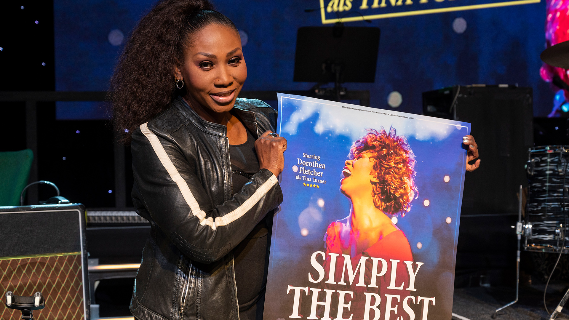 Fletcher steht auf einer Bühne und hält ein Plakat ihrer Show "Simply The Best - Die Tina Turner Story". | dpa