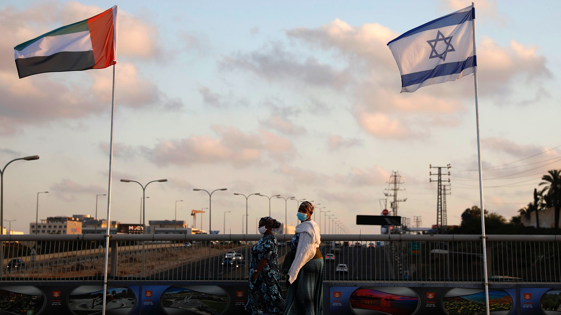 Frauen gehen auf der Friedensbrücke im israelischen Netanja an den Flaggen von Israel und den Vereinigten Arabischen Emiraten vorbei. | AP