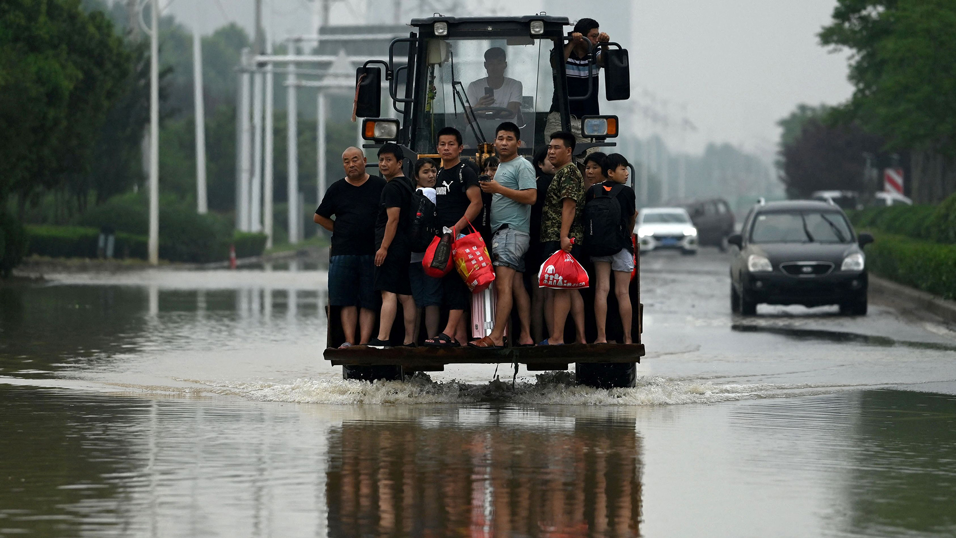 Menschen stehen in Zhengzhou (China) auf einem Radlader, um eine überschwemmte Straße zu überqueren.