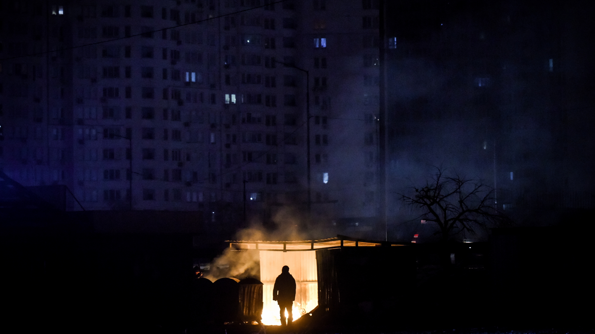 Ein Mann steht in der Nähe von brennendem Müll vor einem Wohnhaus. (Archivbild: 29 November 2022) | EPA