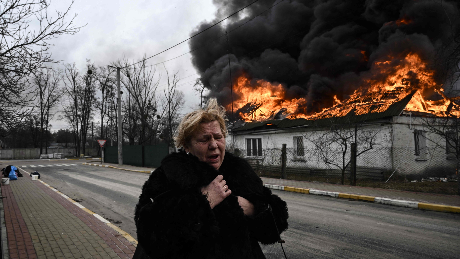 Eine Frau steht vor einem brennenden Haus in Irpin, einem Vorort von Kiew  | AFP