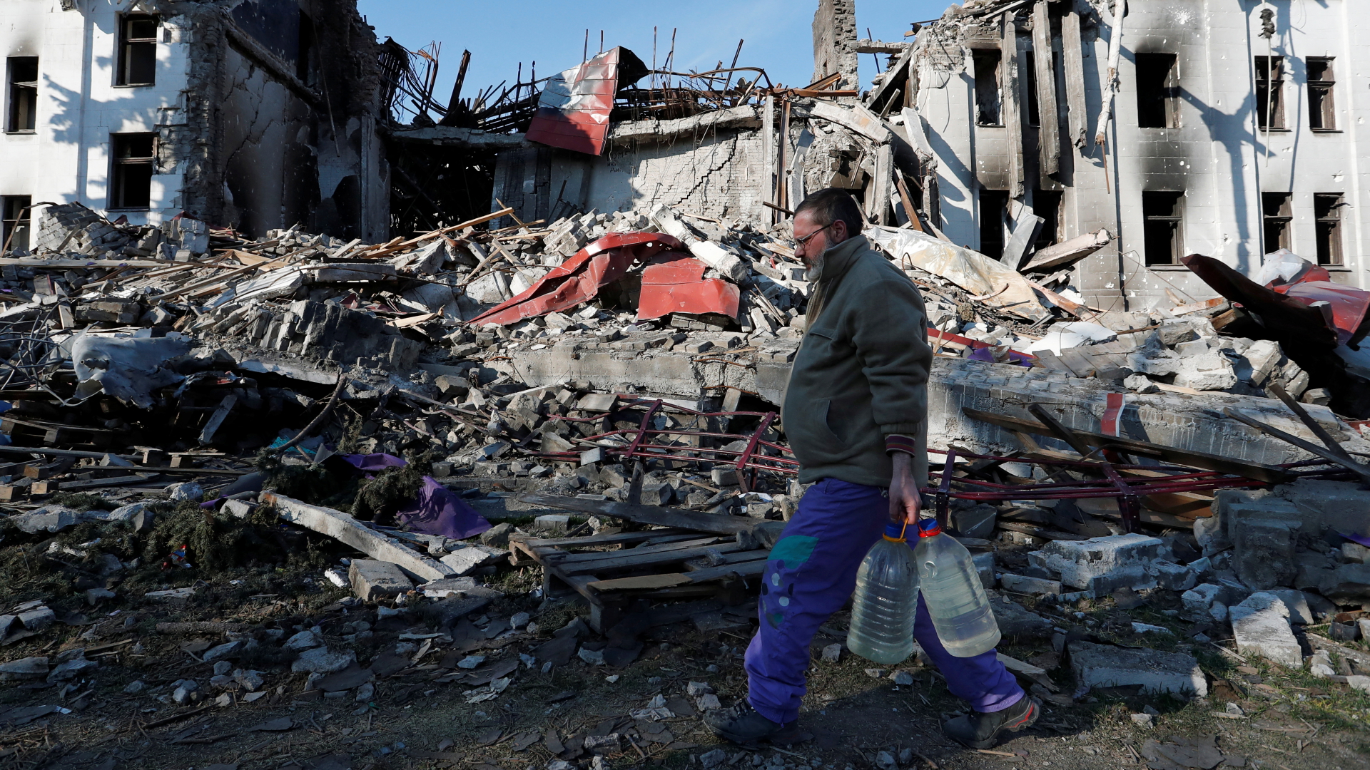 Ein Mann trägt Wasserflaschen durch das vom Krieg zerstörte Mariupol in der Ukraine. | REUTERS