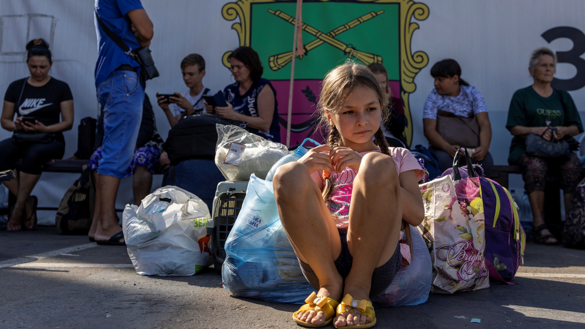 Ein Mädchen sitzt in Saporischschja auf der Straße vor einer Versorgungsstelle für Flüchtlinge zwischen Tüten mit Gepäck. | REUTERS