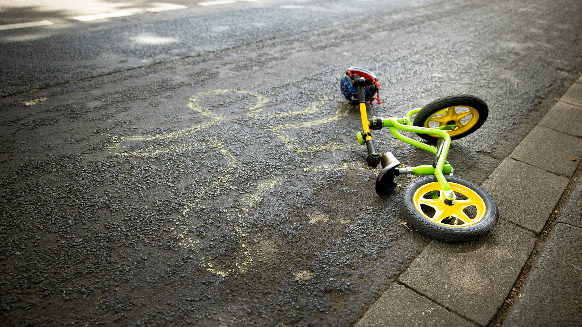 Auf der Straße ist neben einem Laufrad der Umriss eines Kindes gezeichnet.