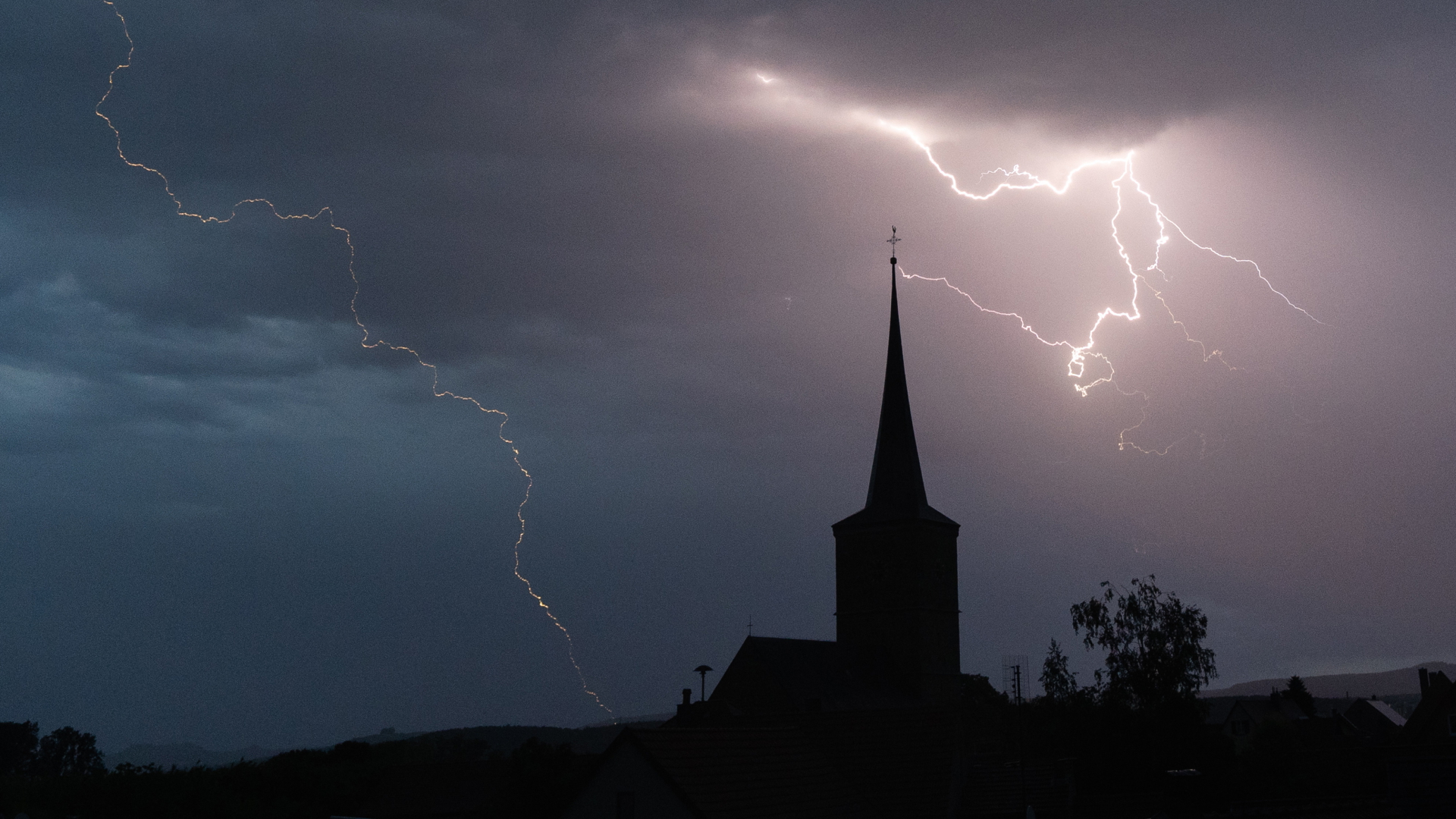 Blitze entladen sich über Rattelsdorf in Bayern, davor die Silhouette eines Kirchturms (Mai 2022).