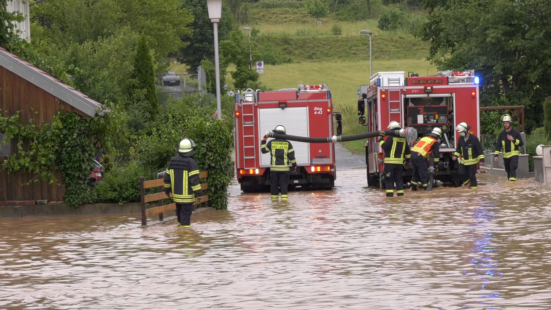 Einsatzkräfte der Feuerwehr stehen auf einer durch ein Unwetter überfluteten Straße im hessischen Breuberg