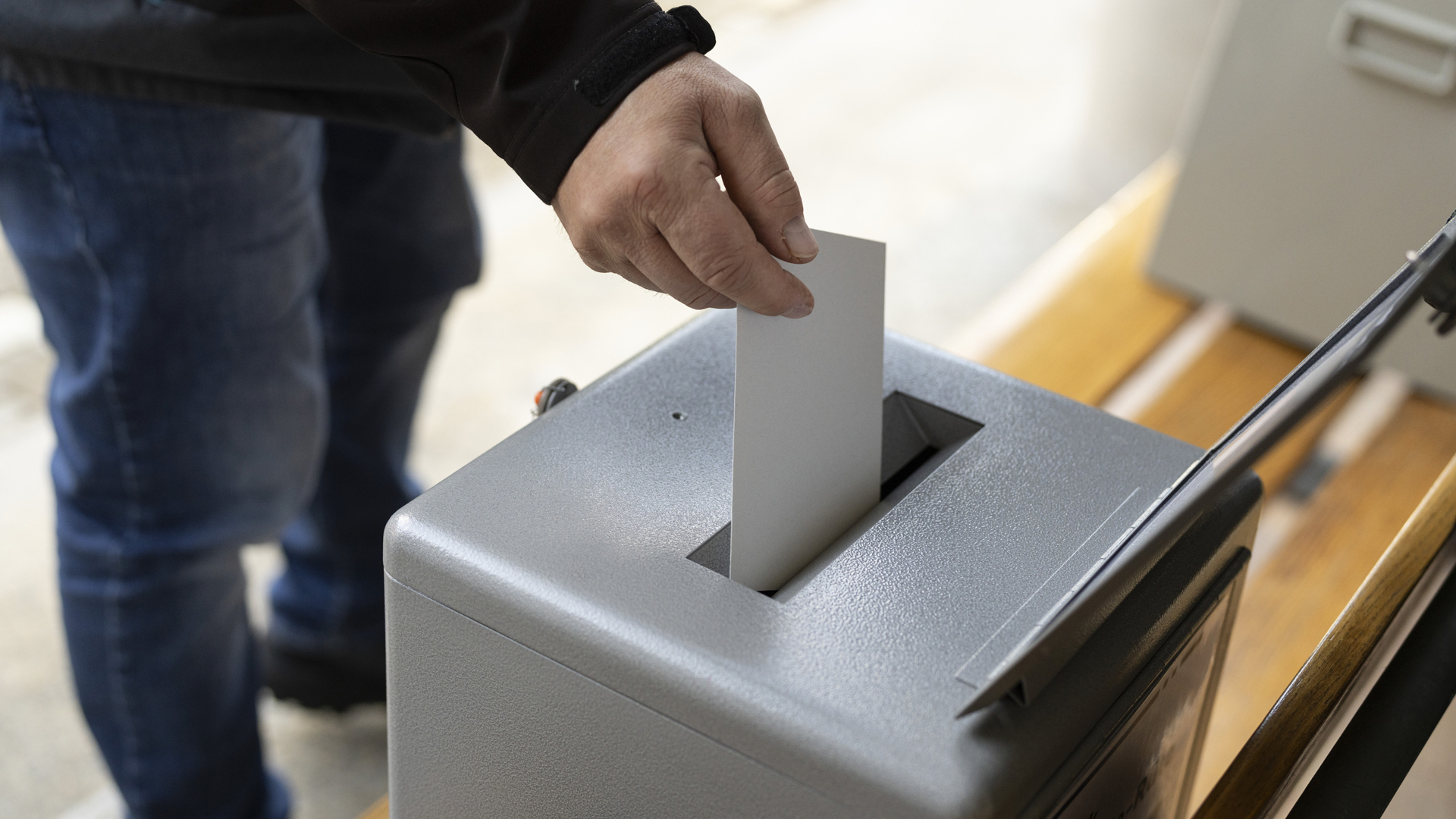 Ein Mann wirft einen Stimmzettel in eine Urne (Nahaufnahme)