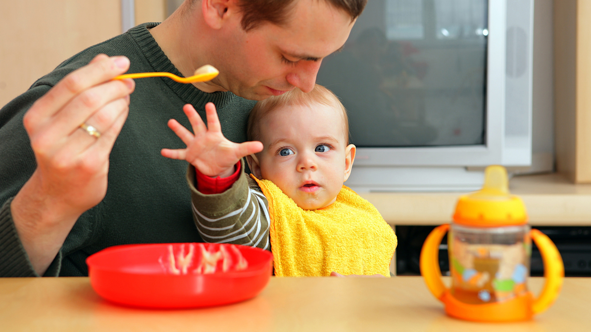 Ein Vater füttert ein Kind. | picture alliance / dpa