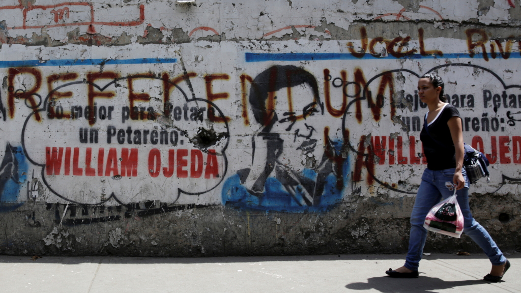Eine Frau läuft an einer Mauer entlang, auf der ein gesprayter Schriftzug das Referendum fordert. | Bildquelle: REUTERS