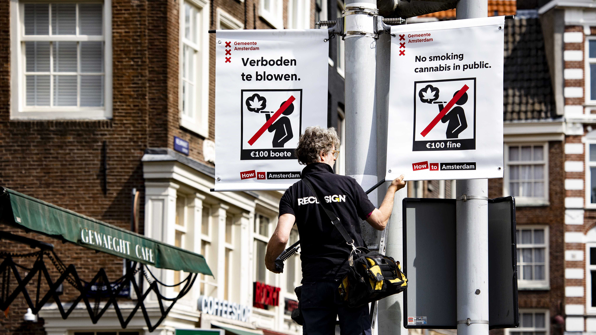 Ein Mitarbeiter platziert ein Verbotsschild in der Innenstadt von Amsterdam - darauf steht u.a. auf englisch: No smoking cannabis in public.
