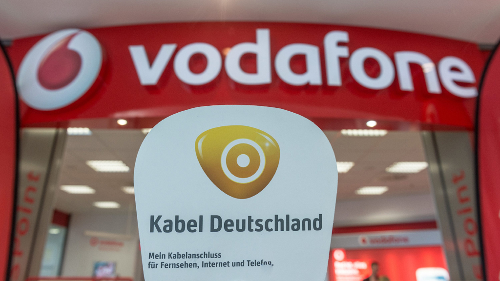 Das Logo des Kabelnetzbetreibers Kabel Deutschland vor dem Schriftzug des Mobilfunkanbieters Vodafone an einem Vodafone-Geschäft, aufgenommen am 17.07.2013 in Regensburg (Bayern).