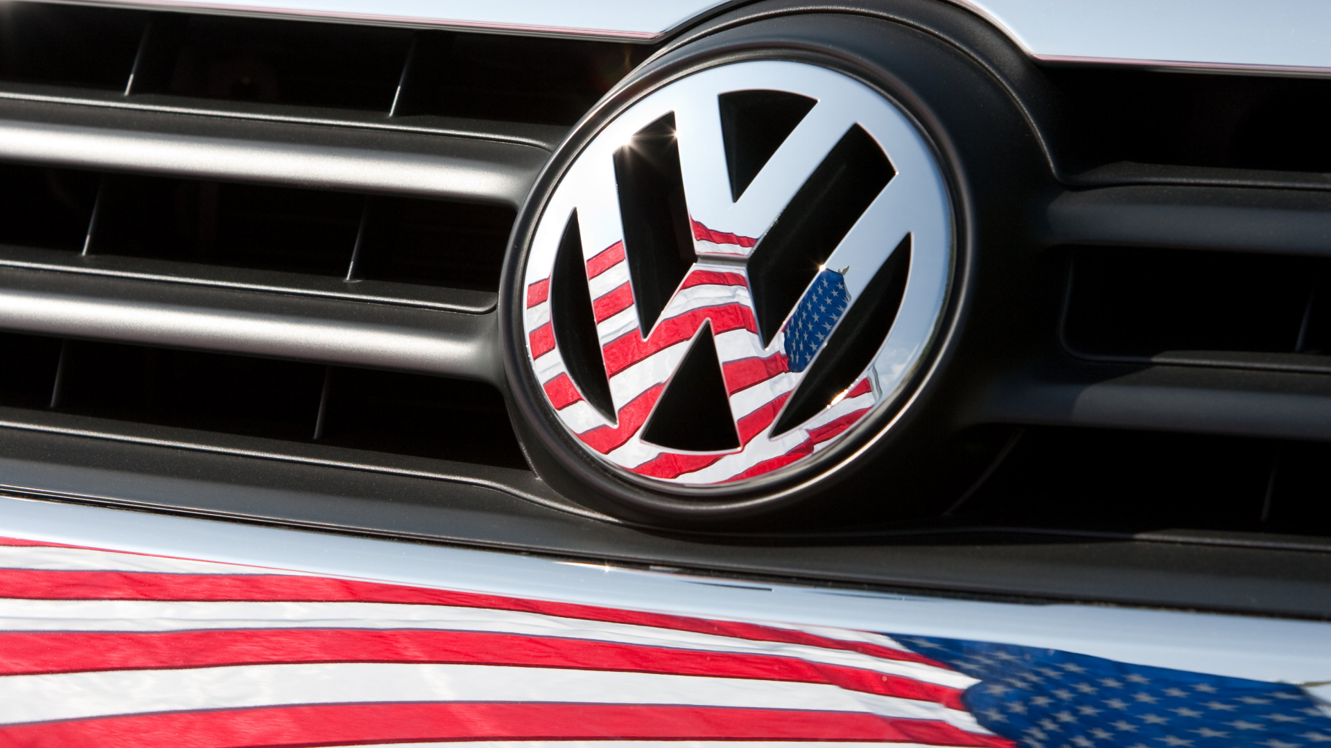 Die amerikanische Fahne spiegelt sich in einem VW-Logo. | dpa