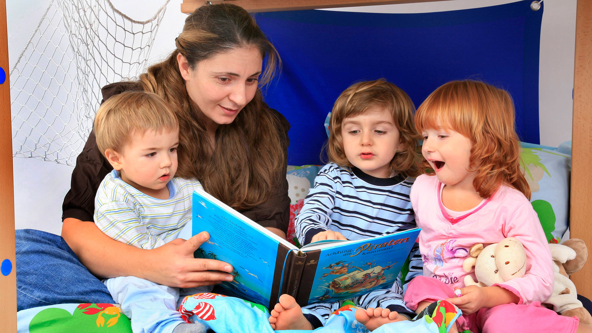 Eine Frau liest drei Kindern aus einem Buch vor. | picture alliance / blickwinkel/f
