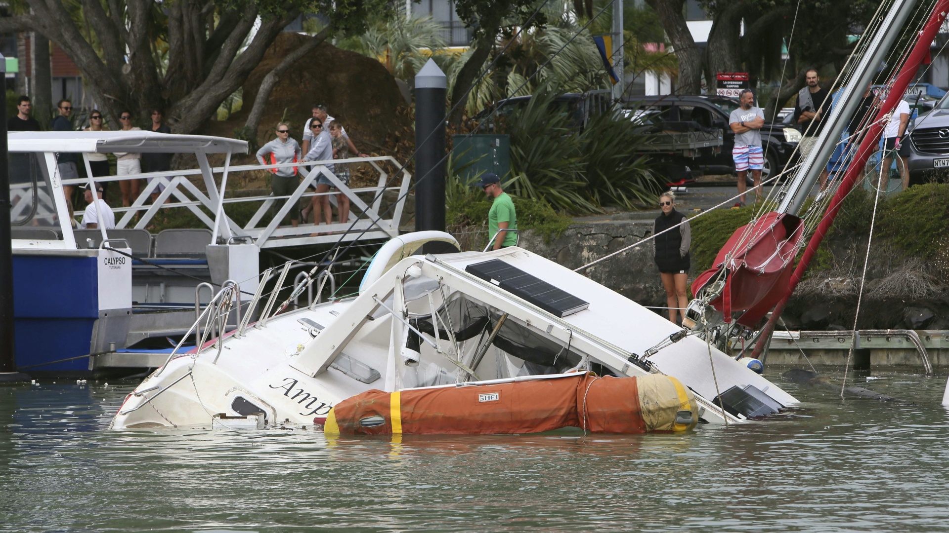 Neuseeland, Tutukaka: Menschen stehen am Hafenbecken und blicken auf ein Boot, das aufgrund starker Flutwellen im Hafen zu sinken droht. | dpa